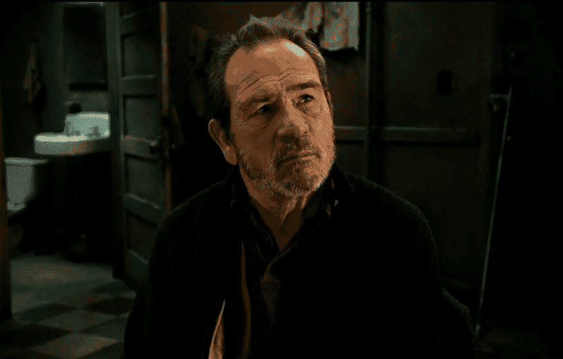Tommy Lee Jones portraying a determined character, dressed casually with a stern look, highlighting his signature tough-guy persona.